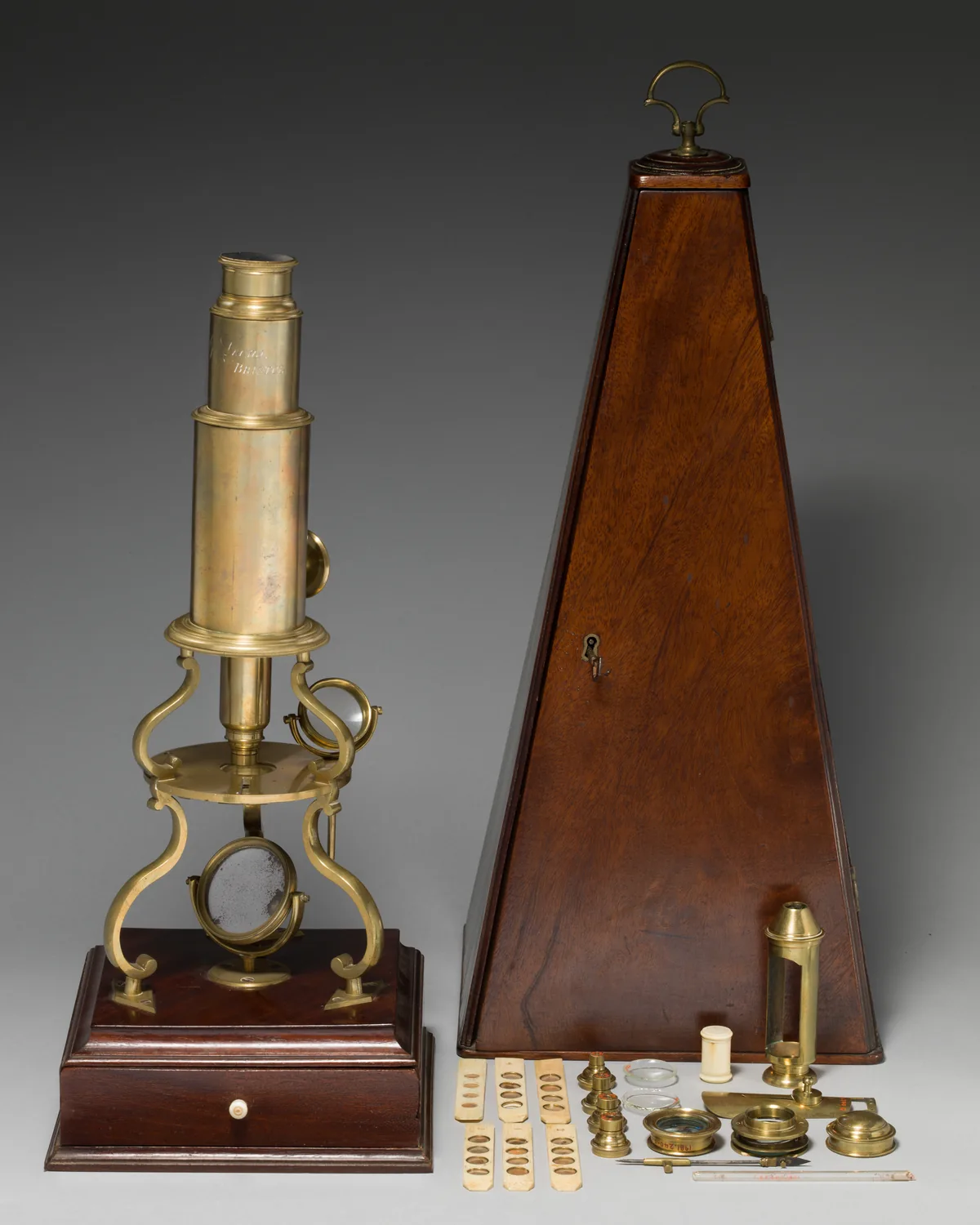 Un microscopio de latón de principios del siglo diecinueve, con su caja de accesorios. Sin un instrumento así nadie hubiera podido ver que el cuerpo está hecho de células: toda la escalera de esta lección depende de poder mirar algo tan pequeño. Imagen del Museo Metropolitano de Arte, dominio público.