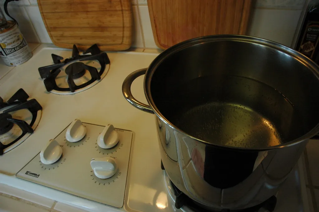 Una olla de metal con agua sobre una hornilla. El calor pasa por conducción: viaja de partícula en partícula a través del metal de la olla hasta llegar al agua, sin que nada se traslade de un lugar a otro como en la convección. Fotografía de Flickr, Wonderlane, licencia BY.