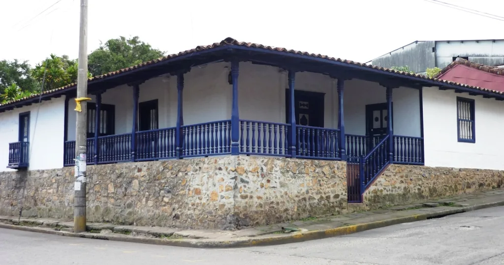 Casa de tipo colonial en Escazú: base de piedra, paredes encaladas, teja de barro y corredor de madera. Sin minas ni grandes fortunas, acá se construyó con lo que había a mano y en una sola planta, y esa forma de casa se siguió levantando mucho después de 1821. Imagen de Wikimedia Commons, Axxis10, CC BY-SA 3.0.
