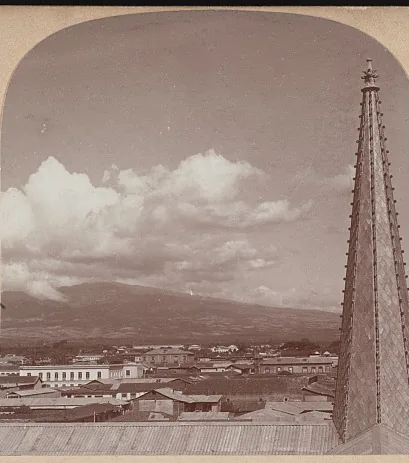 San José vista desde lo alto de un templo a comienzos del siglo XX: techos de teja hasta el horizonte y, al fondo, las montañas que cierran el Valle Central. La ciudad que creció con la plata del café. Vista de una tarjeta estereoscópica de la Biblioteca del Congreso de Estados Unidos, dominio público.