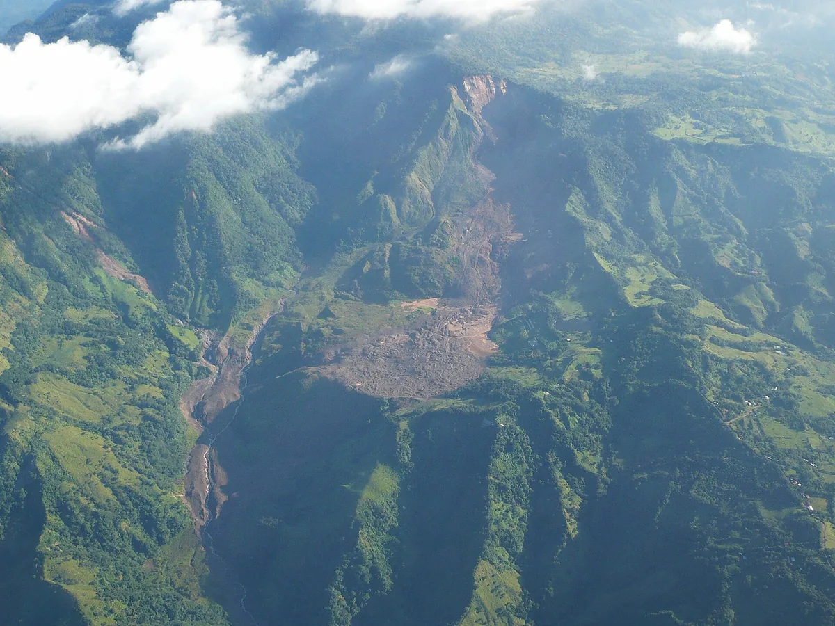 Deslizamiento en la zona del río Aranjuez, en Costa Rica, visto desde el aire en 2008: la ladera se desprendió arriba y el material bajó hasta cubrir el fondo del valle. Un hecho así es donde se pone el dedo para buscar el efecto, y todo lo que quede colgado de él, como el cauce tapado y los potreros cubiertos, sigue siendo consecuencia aunque en el texto aparezca varios renglones después. Fotografía de Hiram Montiel Calderón, Wikimedia Commons, licencia Creative Commons BY-SA 3.0.