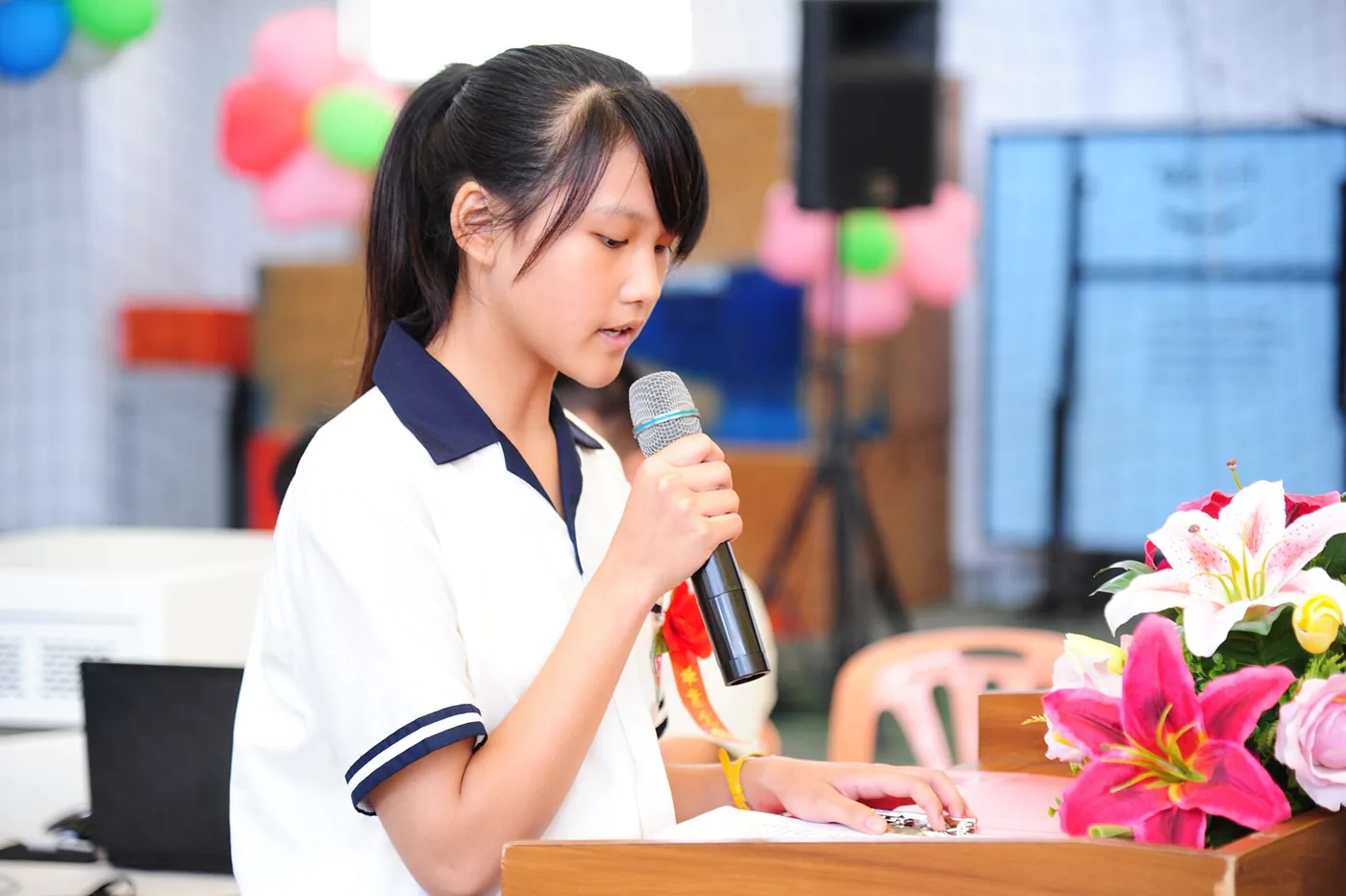 Una estudiante lee su discurso en el acto de graduación: sostiene el micrófono cerca de la boca, apoya el papel y habla despacio. Lo que la lección llama la voz y el cuerpo se ve acá, en la postura y en las manos. Foto: 褒忠國中 雲端網, Wikimedia Commons, CC BY 2.0.