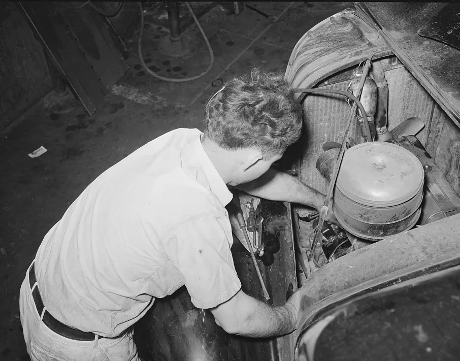 Un mecánico trabaja en el motor abierto de un carro, con las herramientas sobre el guardabarros, en 1939. Édgar se queda mirando un motor abierto igual que este, y ahí es donde conviene no confundirse: la avería es el hecho que desata todo, mientras que el conflicto es que el mismo dinero no alcanza para la reparación y para el alquiler. Fotografía de la Biblioteca del Congreso de Estados Unidos, dominio público.