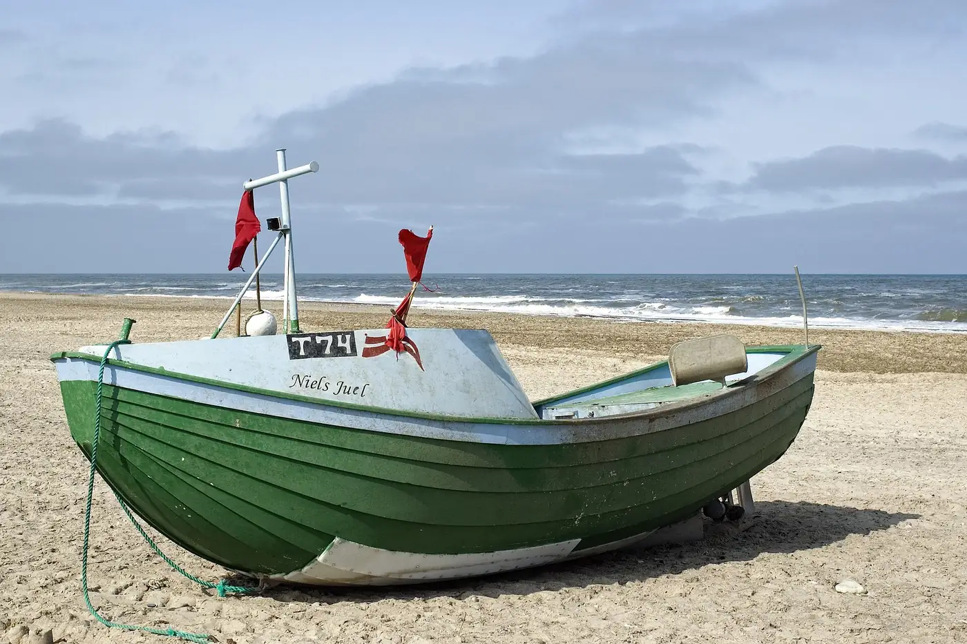Una barca de pesca varada en la arena. En esta escena están casi todas las palabras del campo semántico del mar (ola, arena, barco, gaviota, pescador) y ninguna lleva la raíz mar-, que es lo único que arma una familia léxica. Foto: Mikkel Houmøller, Wikimedia Commons, CC BY-SA 4.0.