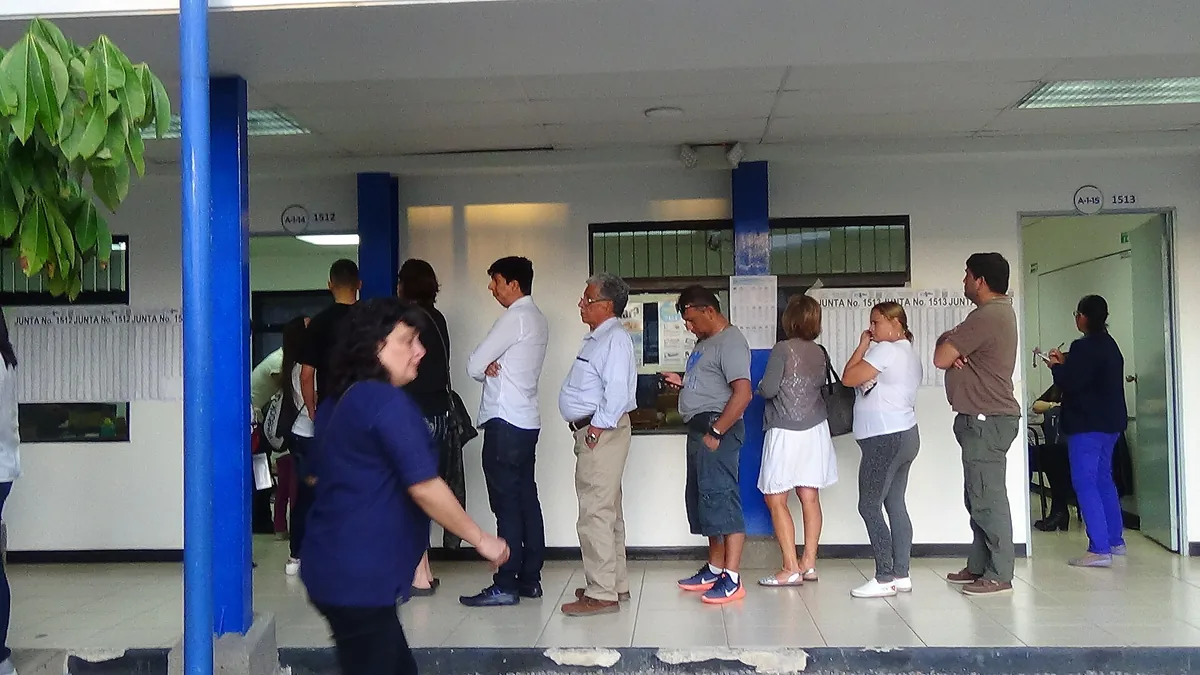 Fila de votantes en una escuela en las elecciones de 2018 en Costa Rica; en la pared van las listas de cada junta receptora. A esa fila solo se entra a los dieciocho, pero participar empieza antes: al comité cantonal de la persona joven se entra desde los doce. Imagen de Wikimedia Commons, Dereck Camacho, CC BY-SA 4.0.