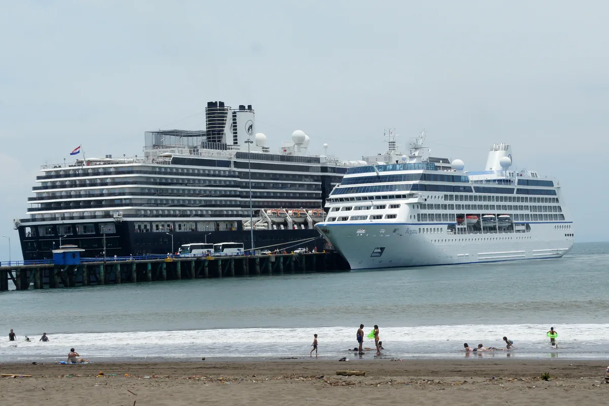 El muelle de Puntarenas, con dos cruceros atracados y gente bañándose en la playa. El mismo puerto que en el siglo XIX sacaba el café hacia el mar hoy vive, sobre todo, del turismo que traen barcos como estos. Foto: Mariordo, Wikimedia Commons (CC BY-SA 3.0).