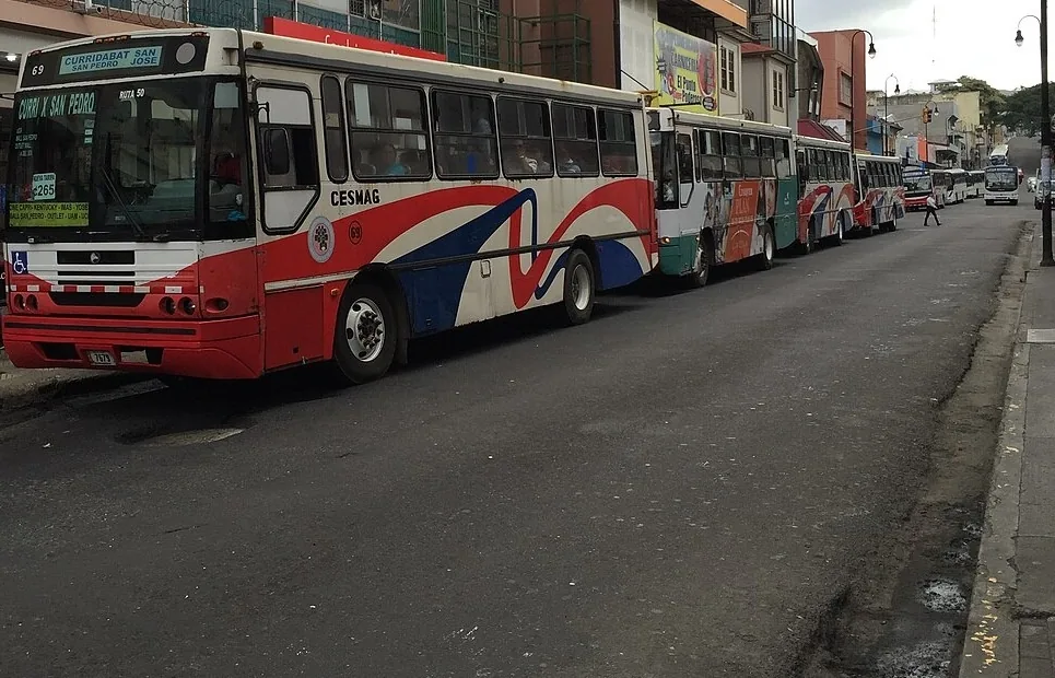 Buses en una calle de San José. Si vas en uno, se dice I go by bus; si vas a pie, I walk. Foto: ArnoldReinhold, Wikimedia Commons, CC BY-SA 4.0 (recortada).