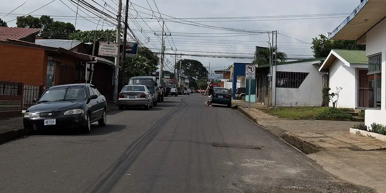 Una calle de barrio en Esparza, Puntarenas: casas, carros parqueados, postes y aceras. Todo eso junto es el neighborhood. Foto: Ll1324, Wikimedia Commons, CC0 (recortada).
