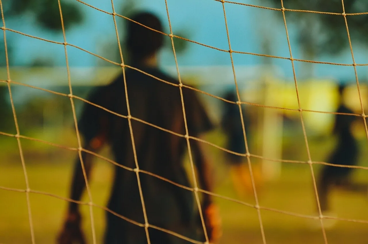 Un portero visto a través de la red del marco. En el fútbol la bola se patea, kick the ball, y el portero intenta atraparla, catch the ball. Foto: Dan Gold, Wikimedia Commons (Unsplash), CC0.