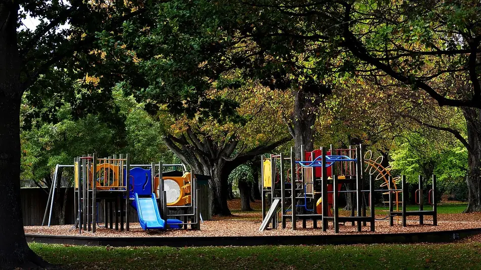 Un play con toboganes y escaleras bajo los árboles. Para contar que te gusta ir ahí se dice I like to go to the playground. Foto: Bernard Spragg, Wikimedia Commons, CC0.