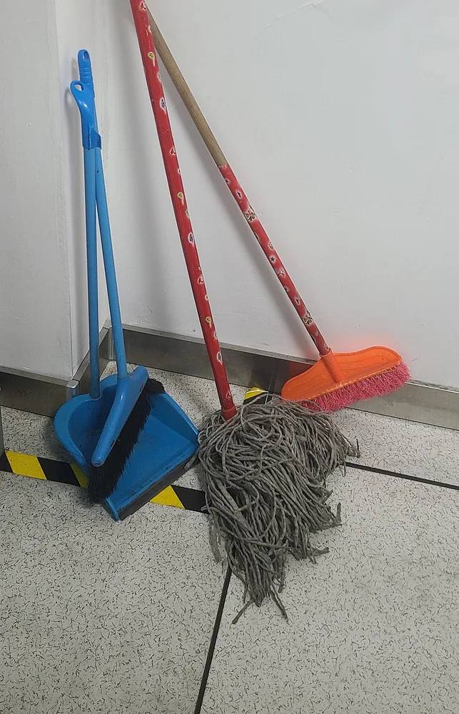 Una escoba, un recogedor y un trapeador apoyados en la pared. En inglés: broom, dustpan y mop. Foto: Nagae Iku, Wikimedia Commons, CC0 (recortada).