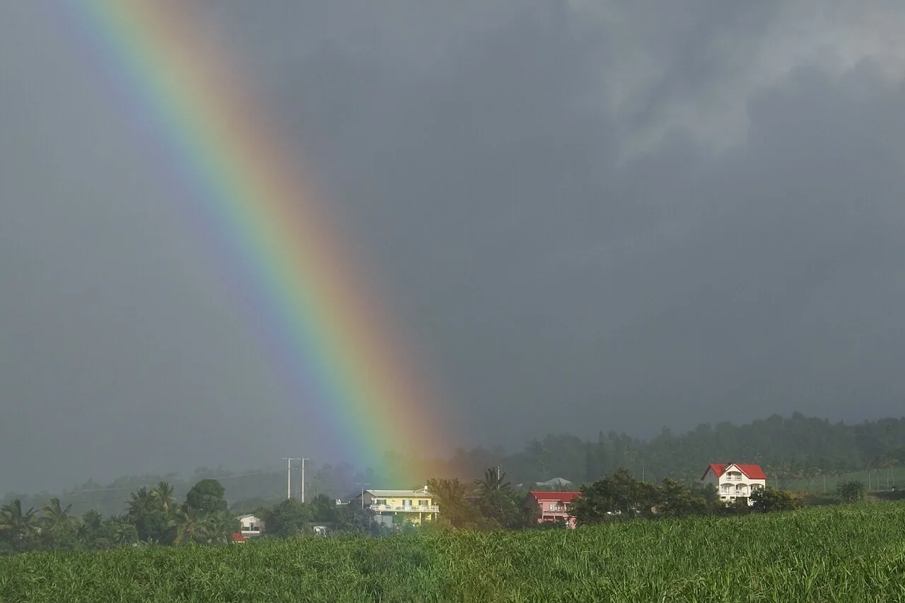 Un arcoíris después de la lluvia sobre un cañal y unas casas. En inglés se llama rainbow. Foto: B.navez, Wikimedia Commons, CC BY-SA 3.0.