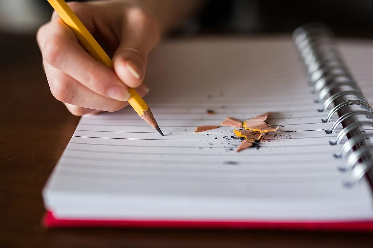 Una mano escribe con lápiz en un cuaderno. Let's write a story! Foto: Thought Catalog, Wikimedia Commons, CC0.