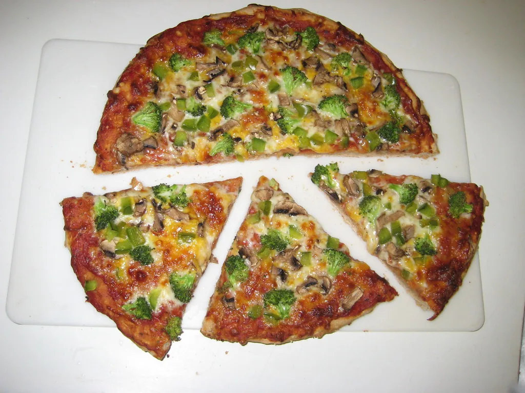 Una misma pizza: arriba quedó media sin cortar y abajo la otra mitad se partió en tres tajadas. Las tajadas de abajo son más chicas porque esa mitad se repartió entre más pedazos, y eso es justo lo que dice el denominador. Por eso, con el mismo numerador, gana la fracción de denominador menor. Imagen de flickr — lgkiii, licencia BY.