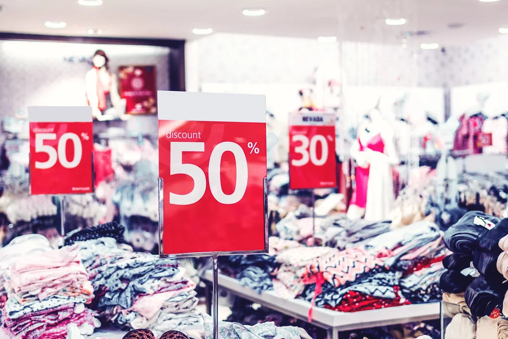 Rótulos de rebaja en una tienda de ropa, con el descuento anunciado en porcentaje. Un 50 % de descuento deja el precio en la mitad y un 30 % lo deja en 70 %: por eso conviene pensar en cuánto queda y multiplicar una sola vez, por 0,50 o por 0,70. El rótulo dice lo que se rebaja, nunca lo que hay que pagar. Imagen de flickr — Artem Beliaikin, licencia CC0.