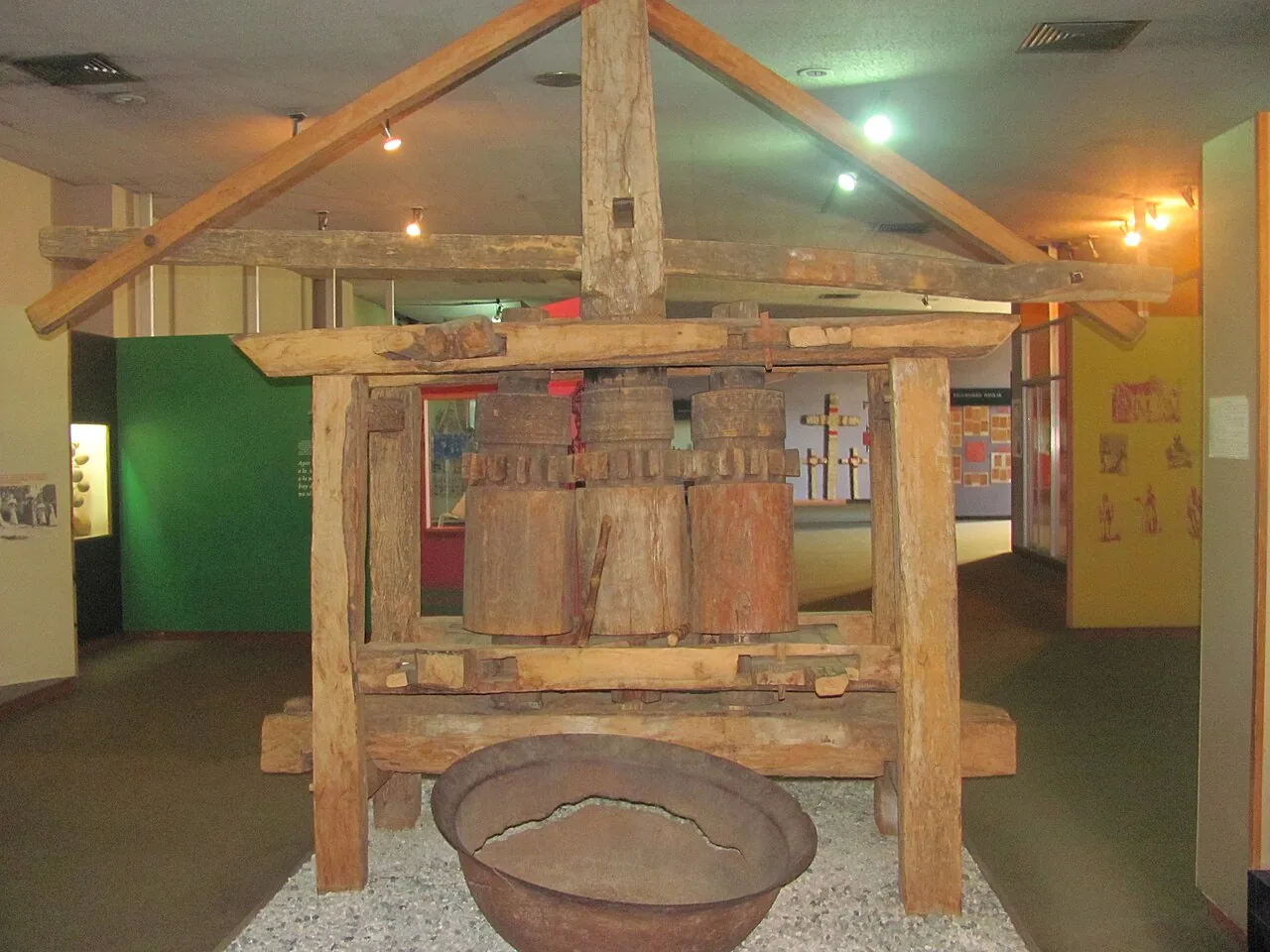 Trapiche antiguo de madera con sus tres rodillos, expuesto en un museo: definirlo pide decir para qué existe, no de qué está hecho ni cómo se mueve. Foto: Caballero1967, Wikimedia Commons, CC BY-SA 4.0.
