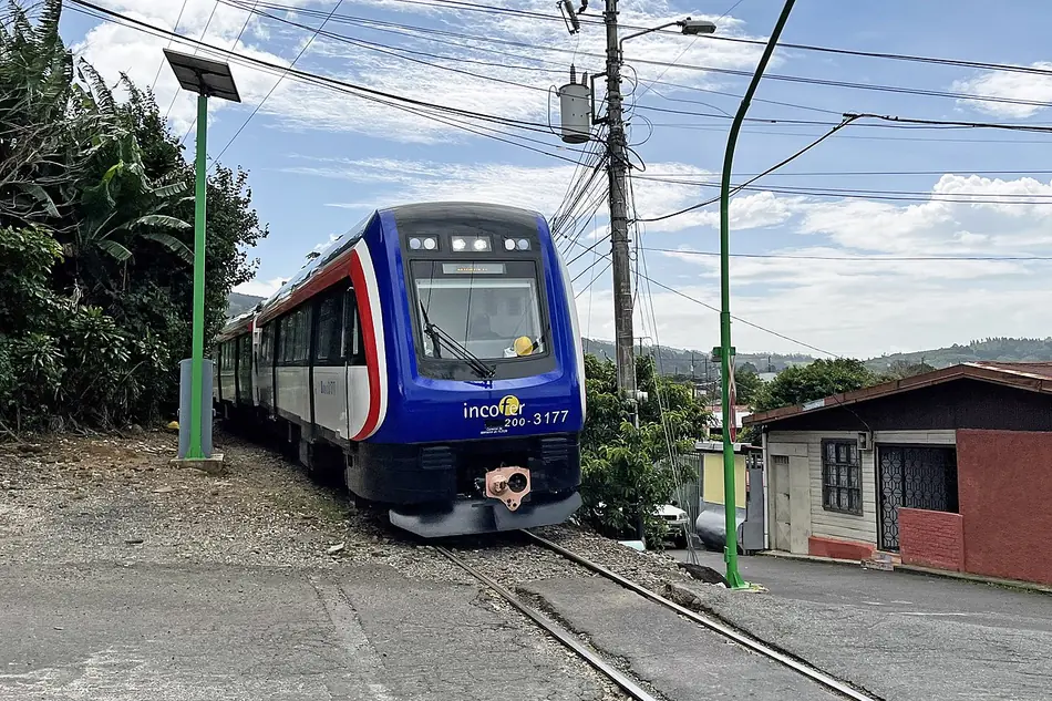 Tren urbano del Incofer cruzando una calle de barrio: su velocidad se piensa en kilómetros por hora, y su horario, en minutos. Foto: Mariordo (Mario Roberto Durán Ortiz), Wikimedia Commons, CC BY-SA 4.0.