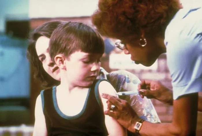 Un niño recibiendo una vacuna en el brazo. La vacuna le enseña al cuerpo a reconocer al microbio antes de que llegue de verdad, y por eso protege sin que uno tenga que enfermarse. Foto: Departamento de Salud de los Estados Unidos, dominio público.